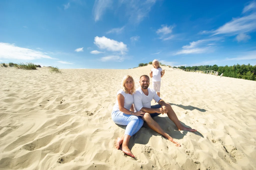 a family of three sit on the sand